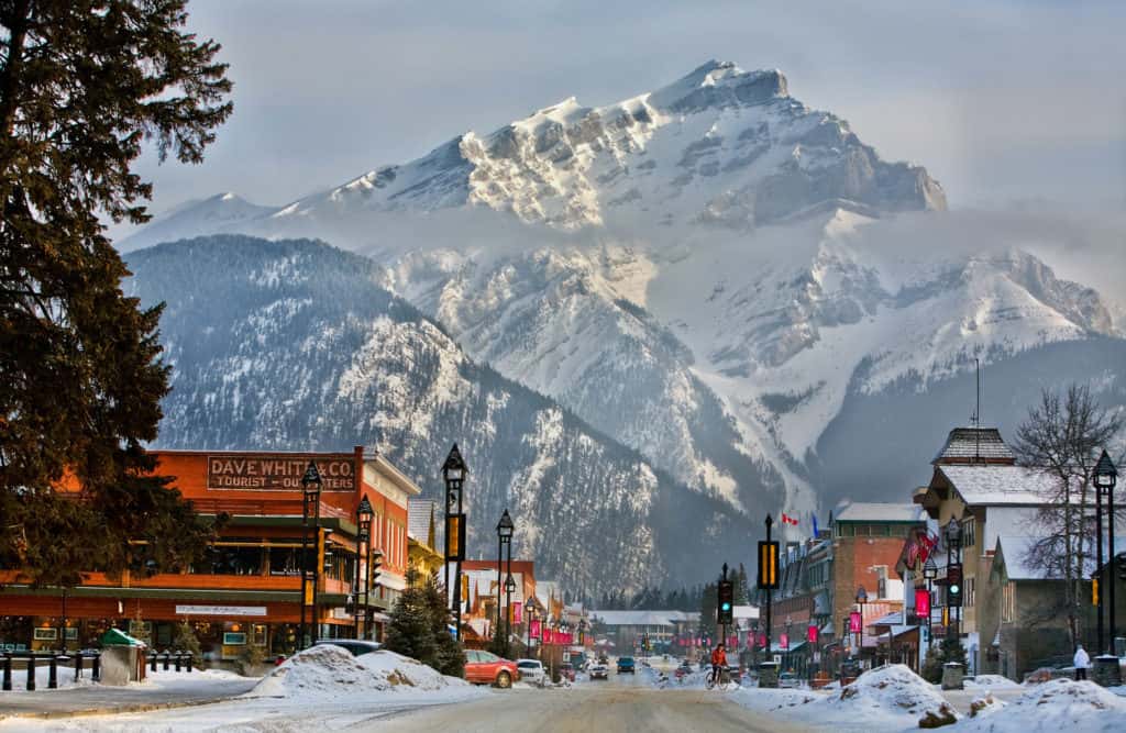 Banff, Canada in November: Events and Activities For 2024 12 Snow-covered Banff Avenue with shops, streetlights, and towering mountains in the background