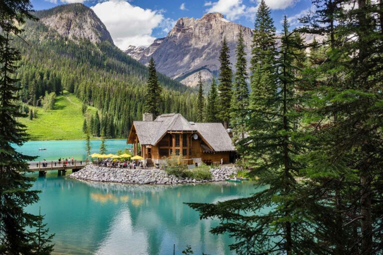 A lakeside lodge with a mountain backdrop, surrounded by lush greenery and turquoise water