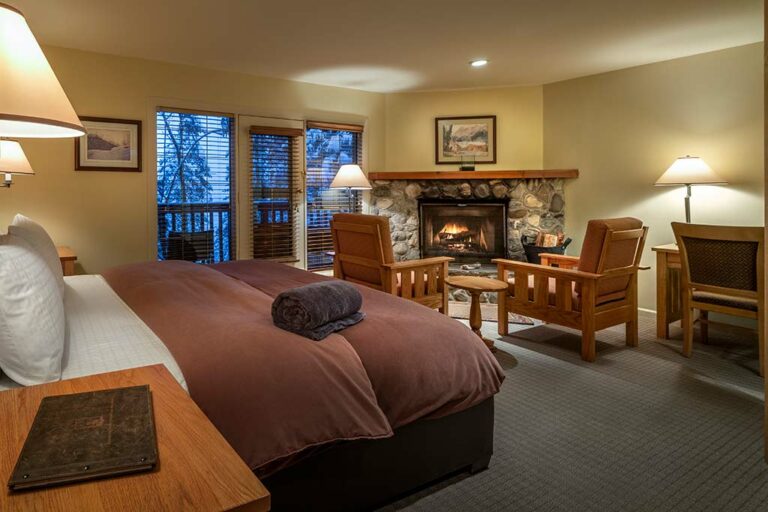 Emerald Lake Lodge room features a stone fireplace, wooden furniture, and a plush bed