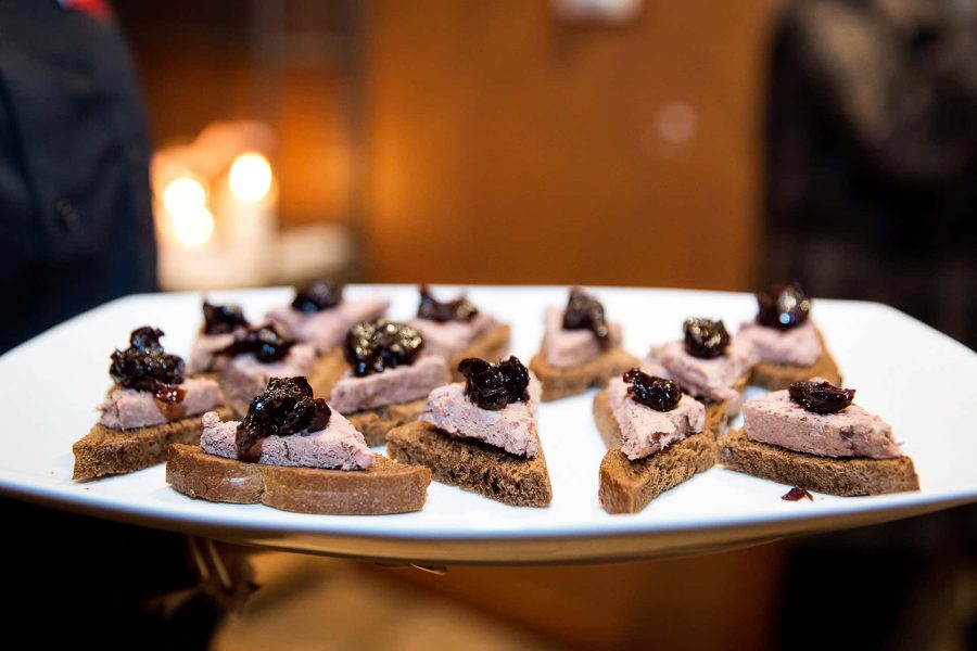 A plate of pate-topped crostini garnished with dark fruit preserves at a catered event