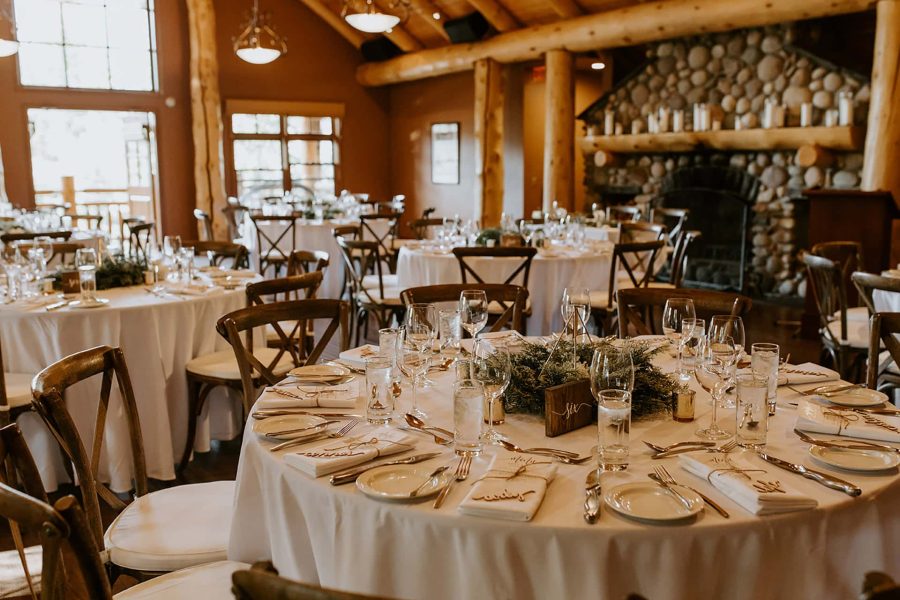 Rustic wedding reception with round tables, white linens, greenery, and a stone fireplace