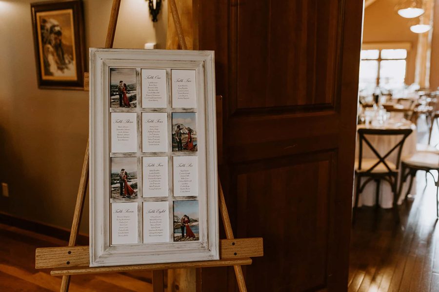 A wedding seating chart in a rustic white frame on an easel, featuring guest names and photos